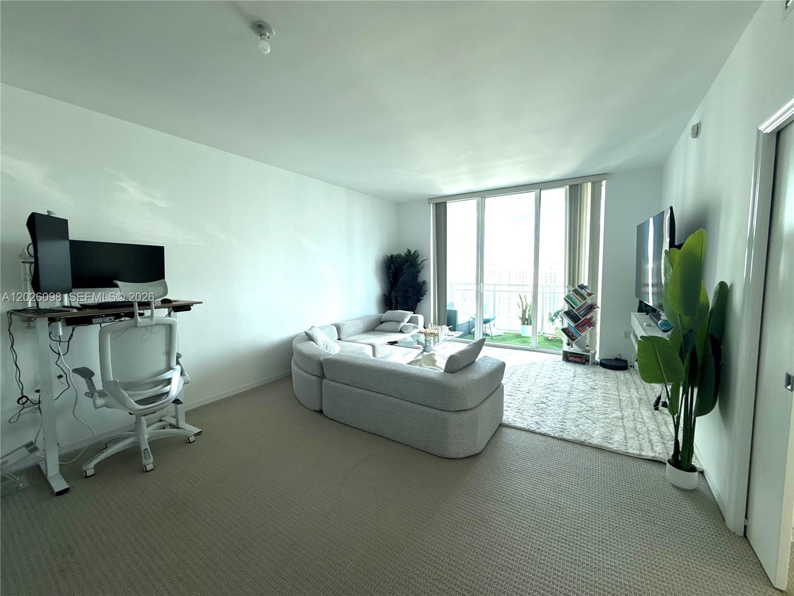 A living room features a curved sofa, a standing desk, and a balcony with views — 951 Brickell Ave # 3703, Miami FL 33131, MIAMI, FL