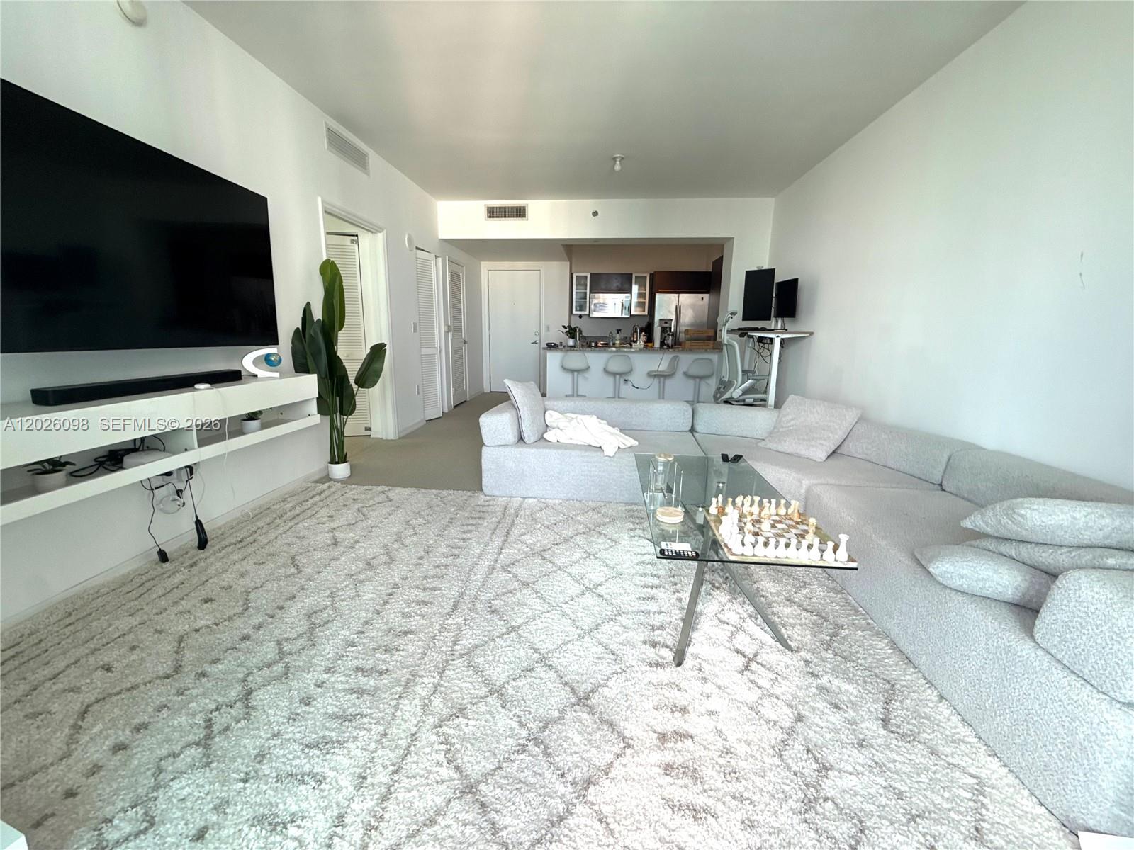 A living room features a large sectional sofa, a glass coffee table, and a television — 951 Brickell Ave # 3703, Miami FL 33131, MIAMI, FL