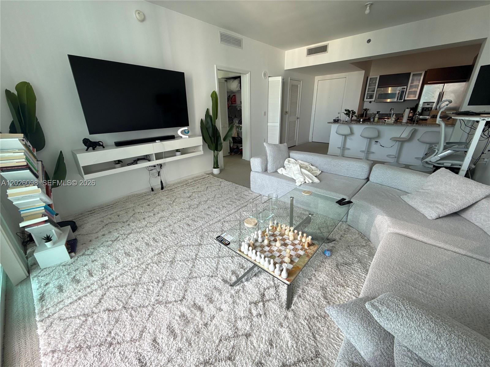 A modern living room features a large sectional sofa, a glass coffee table, and a wall-mounted television — 951 Brickell Ave # 3703, Miami FL 33131, MIAMI, FL
