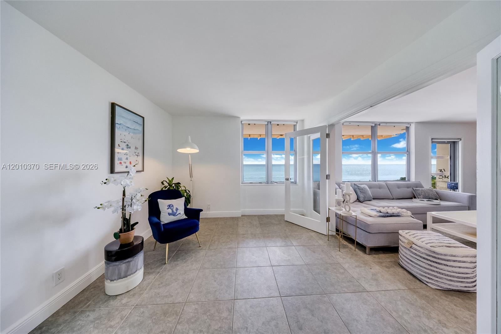 A tiled living room features a blue armchair, a grey sectional, and ocean views — 9225 Collins Ave # 501, Surfside FL 33154, SURFSIDE, FL