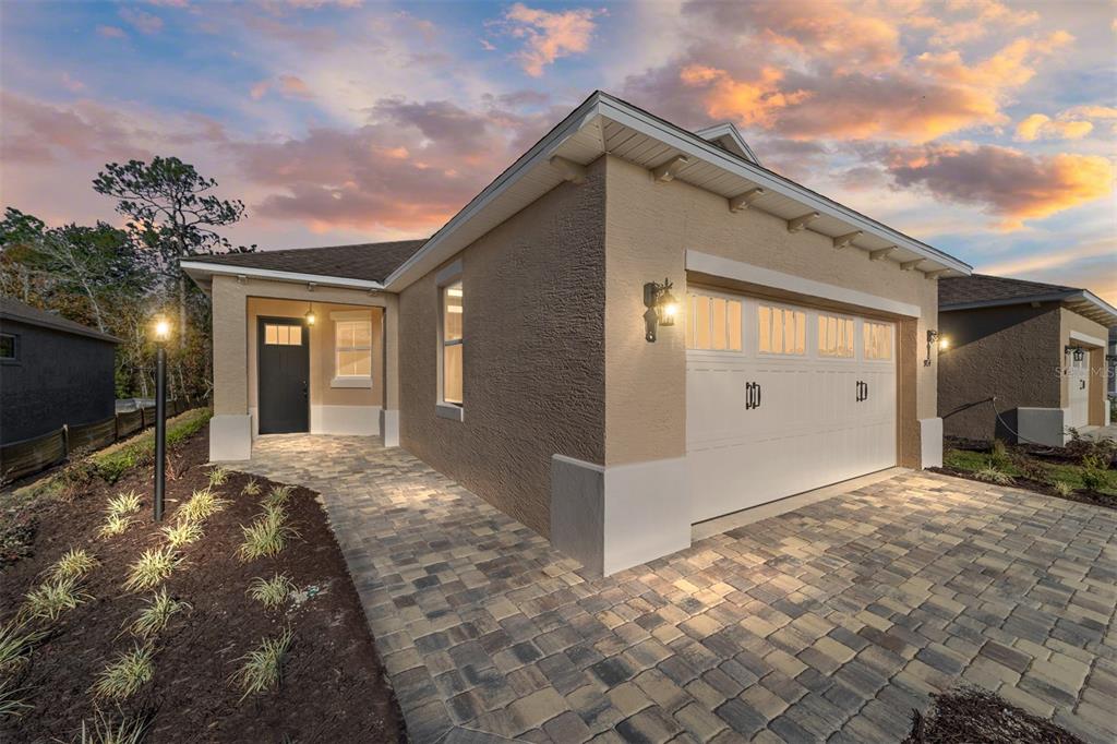 A beige single-story house with a white garage door and a paved walkway at sunset — 9714 SW 108TH TERRACE ROAD, OCALA, FL