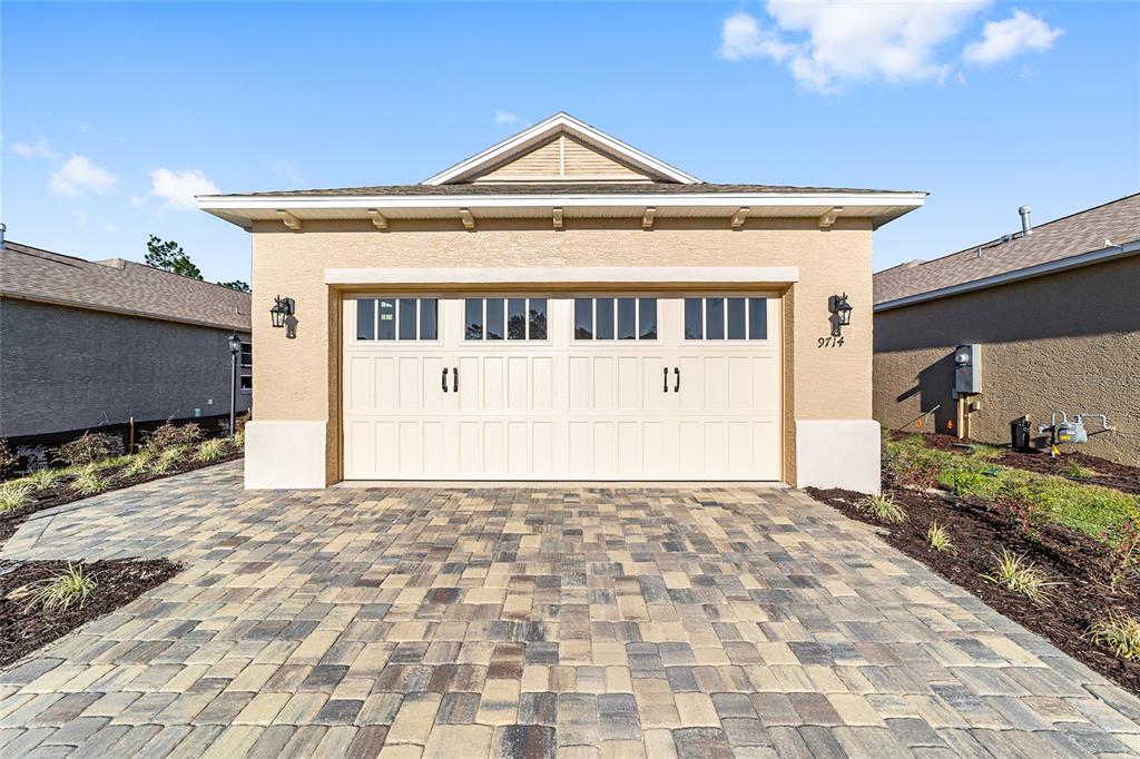 A beige detached garage with a paver driveway and a white two-car garage door — 9714 SW 108TH TERRACE ROAD, OCALA, FL