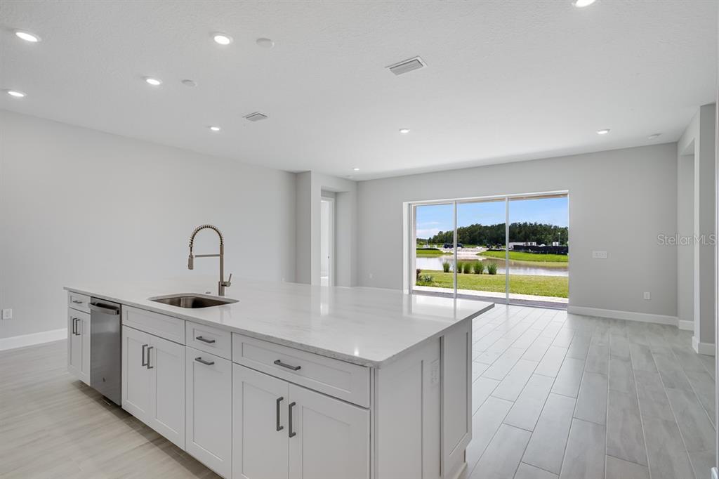 A modern white kitchen features a large island, stainless steel appliances, and light wood flooring — 5652 NEVIS TERRACE, KISSIMMEE, FL