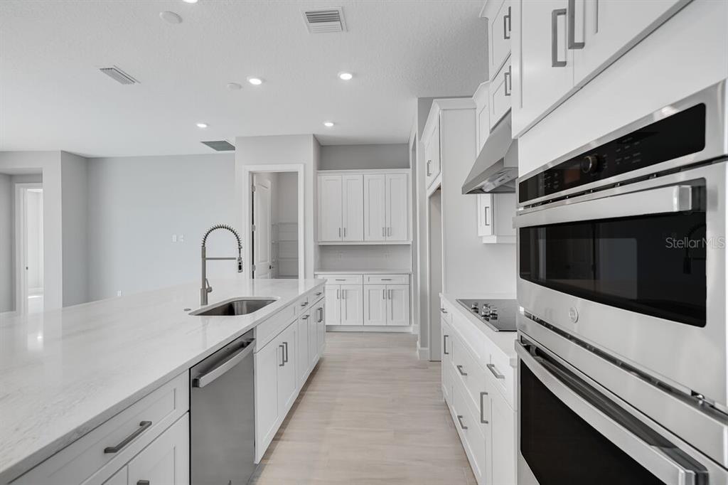 A modern white kitchen features a large center island, stainless steel appliances, and light flooring — 5652 NEVIS TERRACE, KISSIMMEE, FL