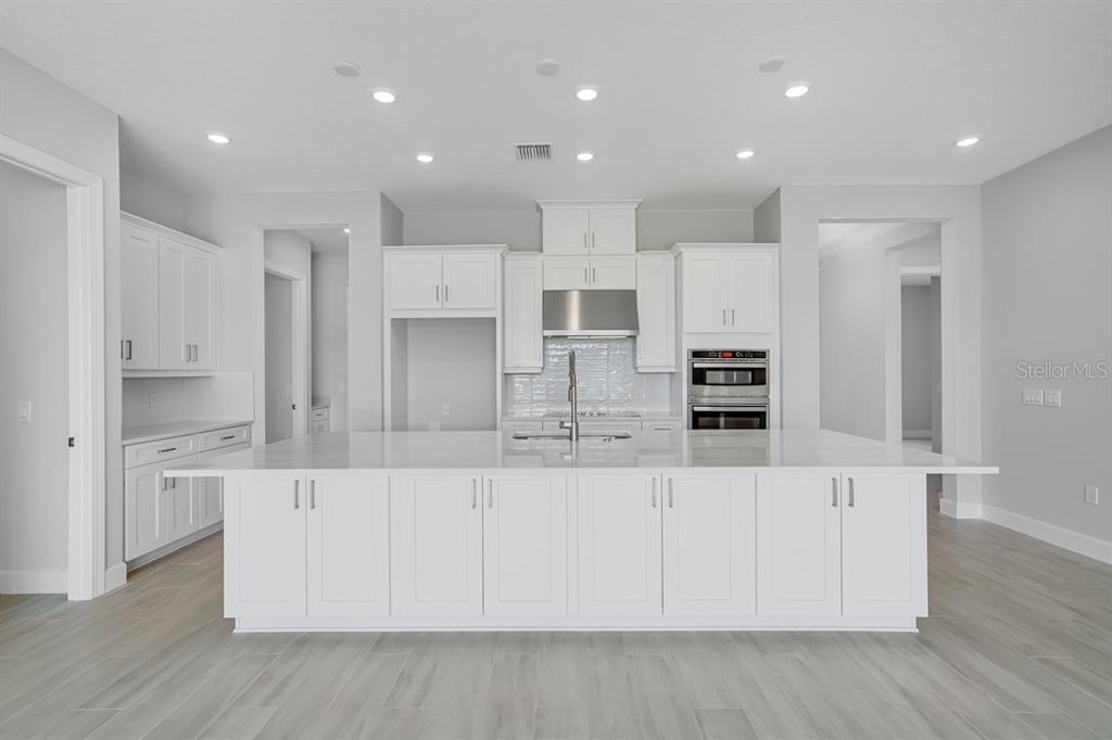 A modern kitchen features white cabinetry, a large island with a sink, and stainless steel appliances — 5652 NEVIS TERRACE, KISSIMMEE, FL