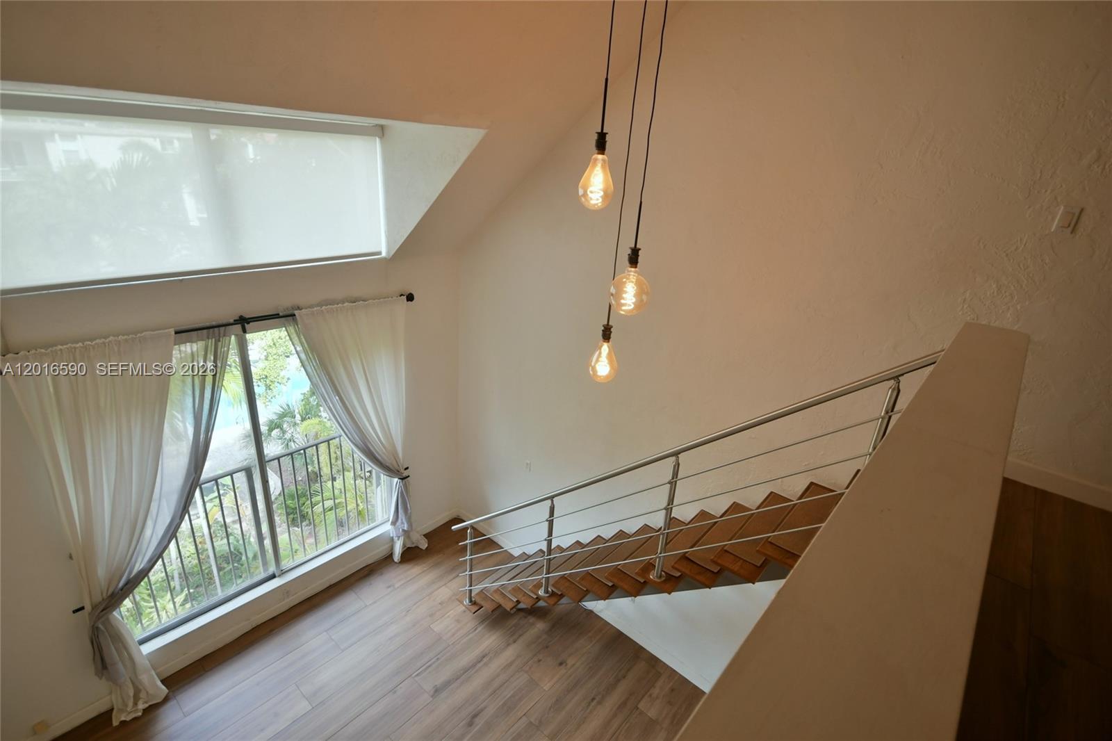 A high-ceilinged room features a wooden staircase with a metal railing and pendant lighting — 6884 N Kendall Dr # C401, Pinecrest FL 33156, PINECREST, FL