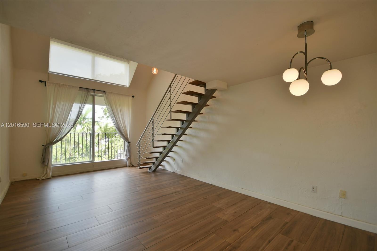 A living room features wood-look flooring, a floating staircase, and a large window with curtains — 6884 N Kendall Dr # C401, Pinecrest FL 33156, PINECREST, FL