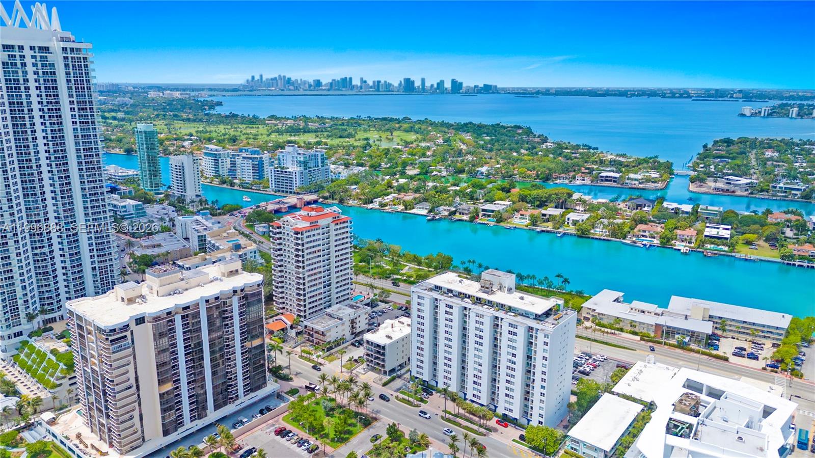An aerial view shows high-rise apartment buildings situated along a canal near a bay — 6450 Collins Ave # 204, Miami Beach FL 33141, MIAMI BEACH, FL