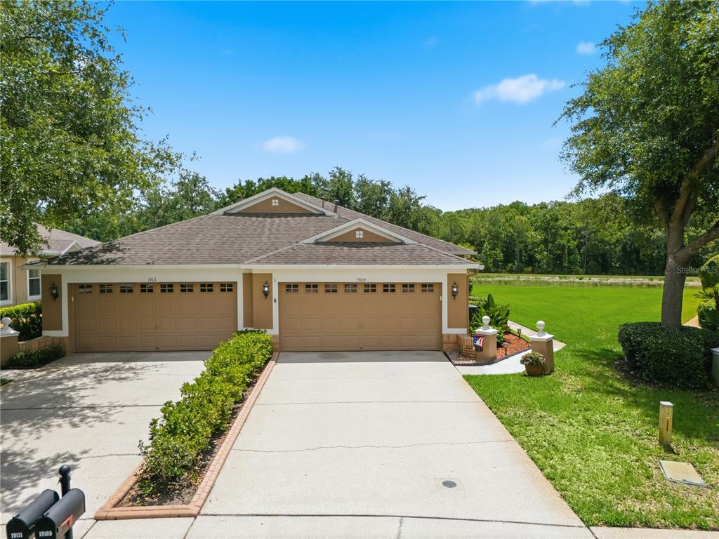 A duplex house with two tan garage doors and a shared driveway under a blue sky — 19109 WHITE WING PLACE, TAMPA, FL