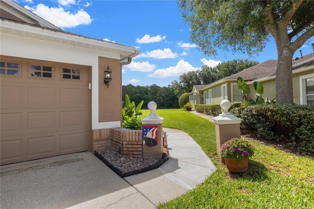 A tan garage with a concrete driveway and a walkway leading to a landscaped yard — 19109 WHITE WING PLACE, TAMPA, FL