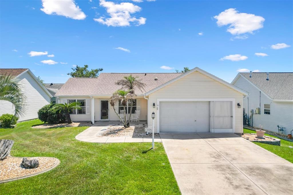 A single-story house with light siding, a front-facing garage, and a landscaped front yard — 1910 AUGUSTINE DRIVE, THE VILLAGES, FL