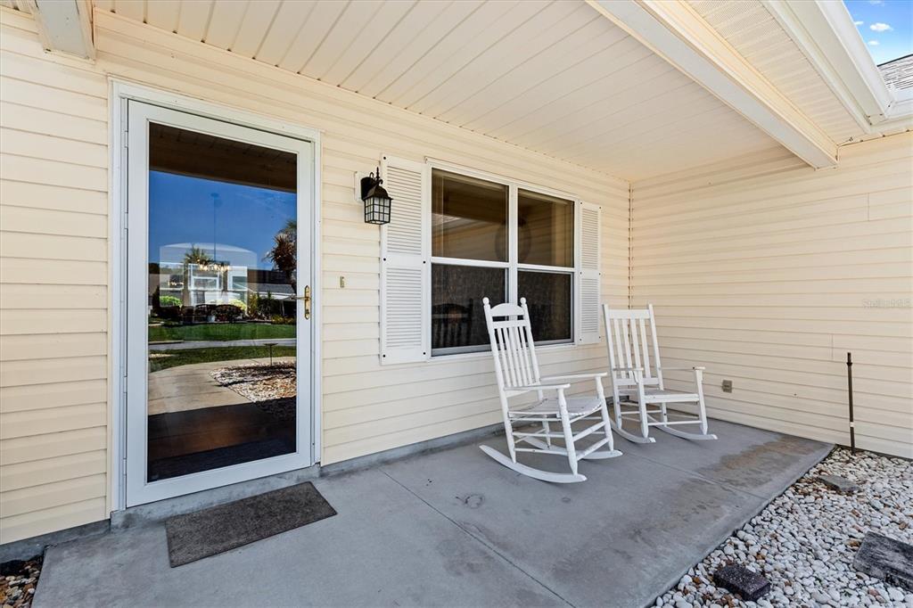 A covered front porch features light siding, a glass storm door, and two white rocking chairs — 1910 AUGUSTINE DRIVE, THE VILLAGES, FL