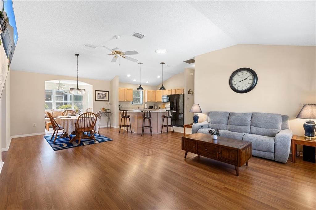 An open-concept living room and kitchen feature light wood flooring, a gray sofa, and cabinetry — 1910 AUGUSTINE DRIVE, THE VILLAGES, FL