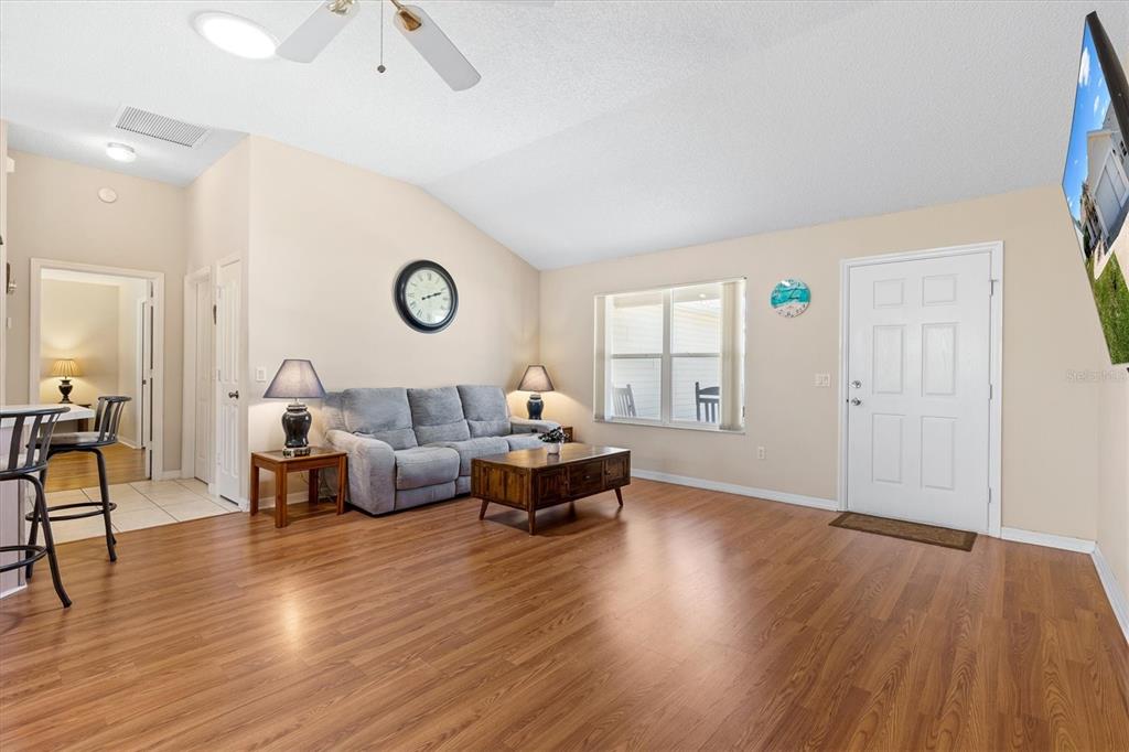 A living room features wood-look flooring, a gray sofa, a coffee table, and a front door — 1910 AUGUSTINE DRIVE, THE VILLAGES, FL
