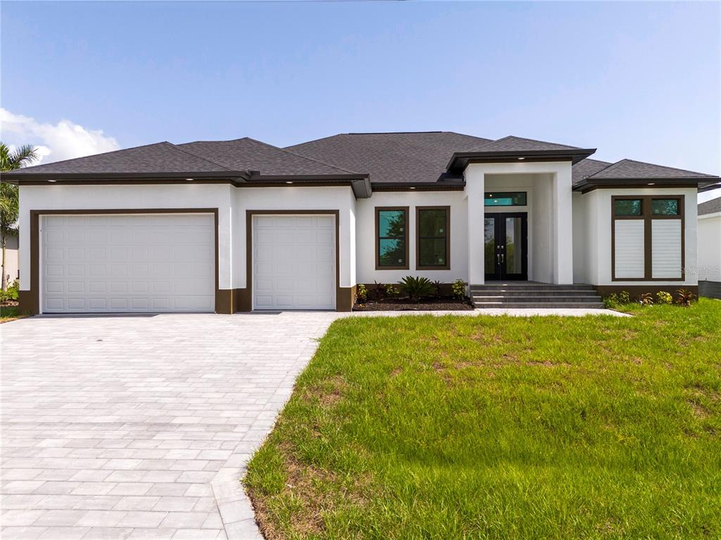 A modern single-story house with a white exterior, dark trim, and a three-car garage — 14958 WICHITA ROAD, PORT CHARLOTTE, FL