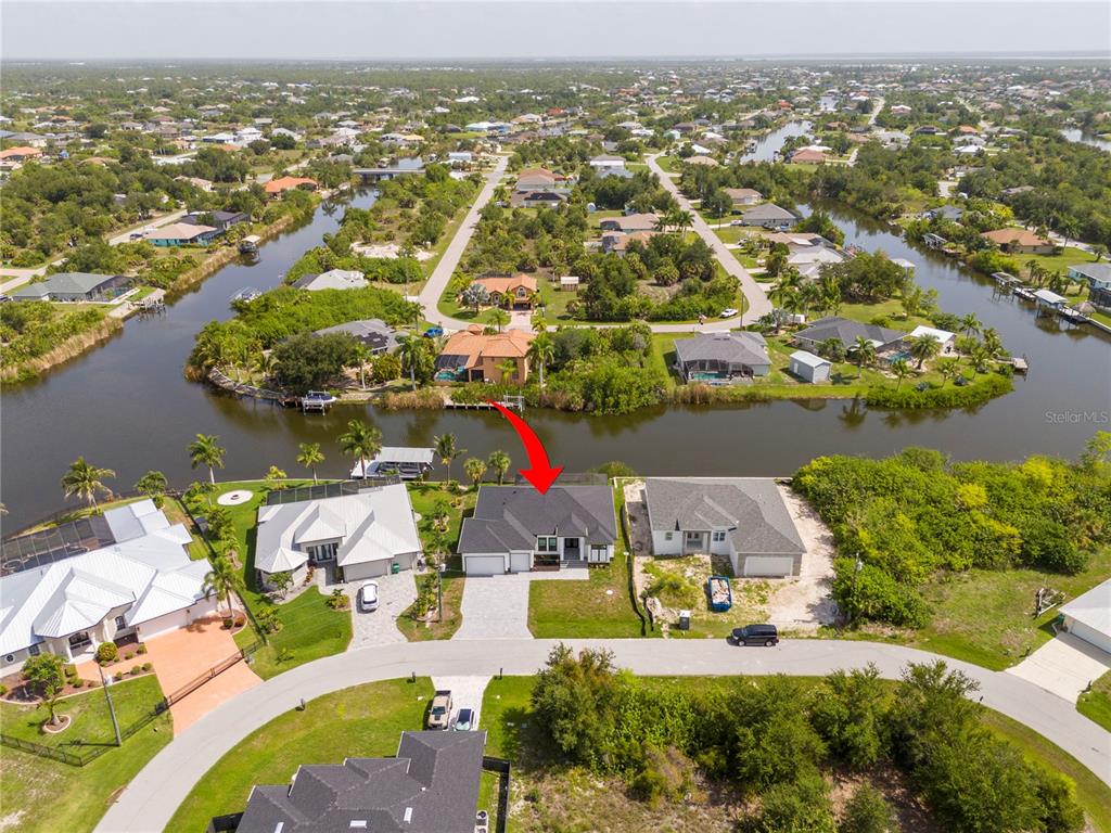 An aerial view shows a waterfront house with a red arrow pointing to its roof — 14958 WICHITA ROAD, PORT CHARLOTTE, FL