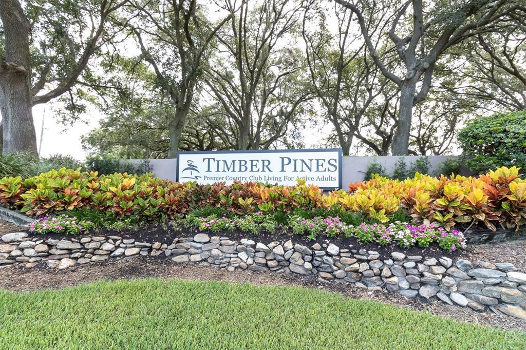 A stone retaining wall sits in front of a Timber Pines community entrance sign — 7099 POND VIEW COURT, SPRING HILL, FL