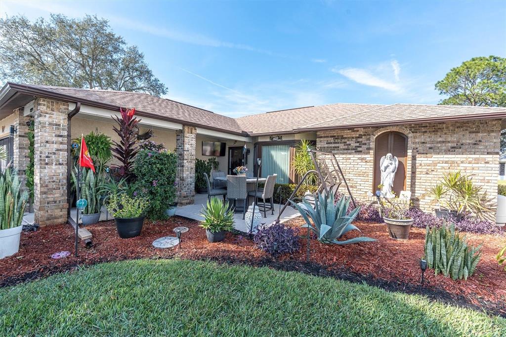 The exterior of a brick house features a covered patio, landscaping, and a lawn — 7099 POND VIEW COURT, SPRING HILL, FL