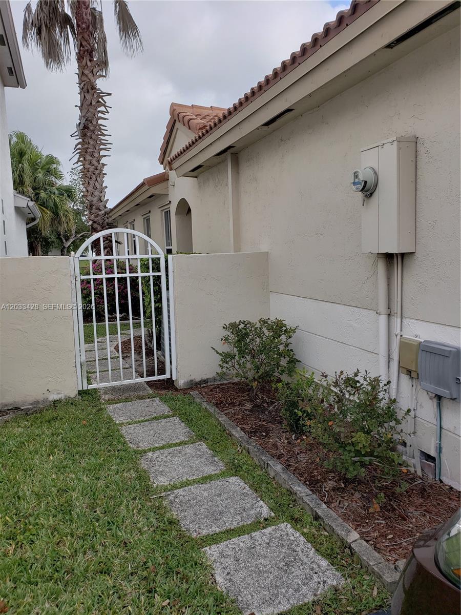 A white metal gate leads to a side yard along the exterior of a house — PEMBROKE PINES, FL