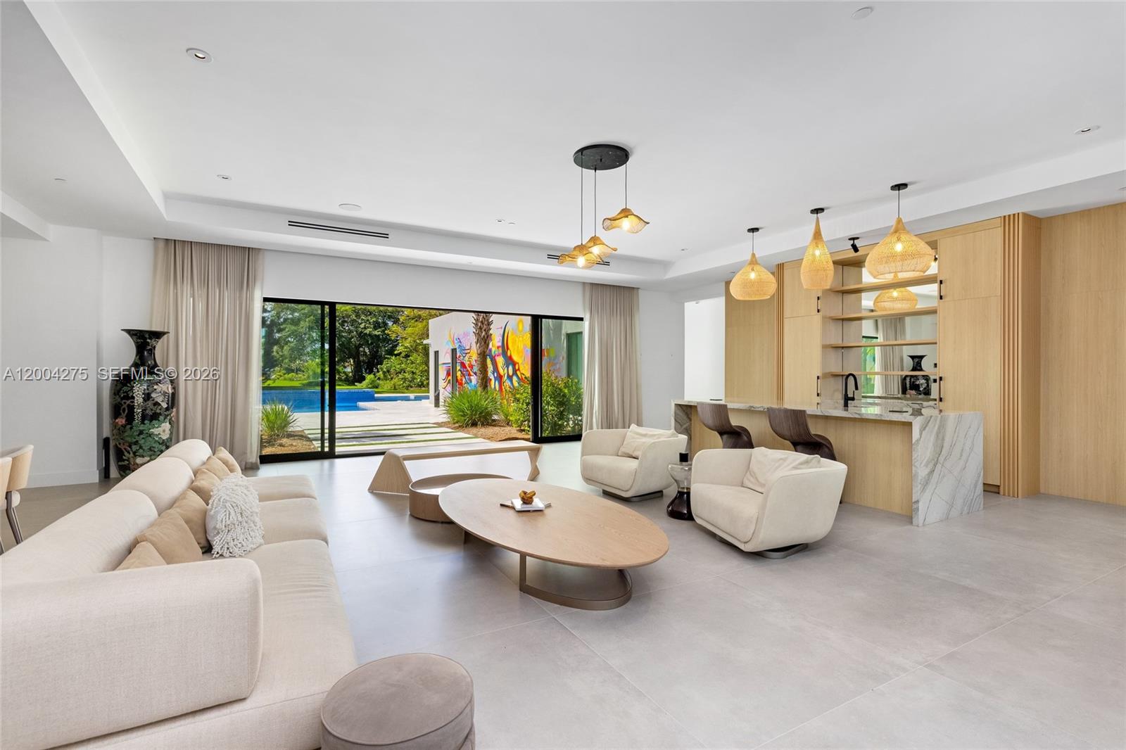 A modern living room features a bar, neutral furniture, and large sliding doors to a pool — 5700 Cypress Rd, Plantation FL 33317, PLANTATION, FL