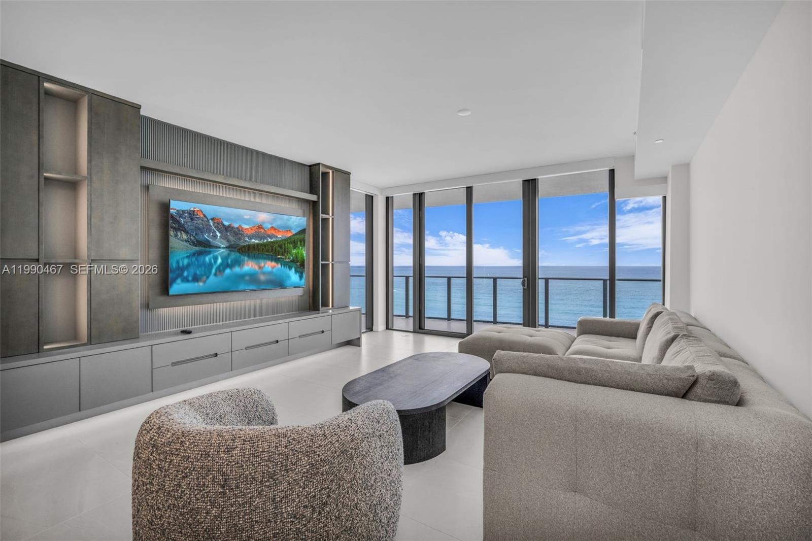 A modern living room features a large media wall, gray sofa, and floor-to-ceiling ocean views — 1116 N Ocean Blvd # 1106, Pompano Beach FL 33062, POMPANO BEACH, FL