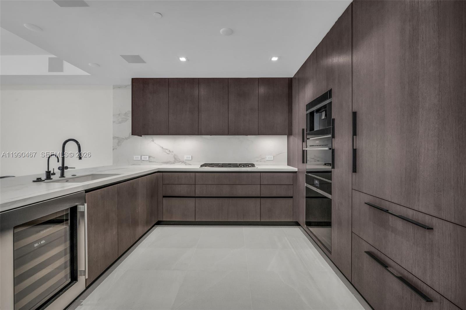A modern kitchen features dark wood cabinetry, marble countertops, and stainless steel appliances — 1116 N Ocean Blvd # 1106, Pompano Beach FL 33062, POMPANO BEACH, FL