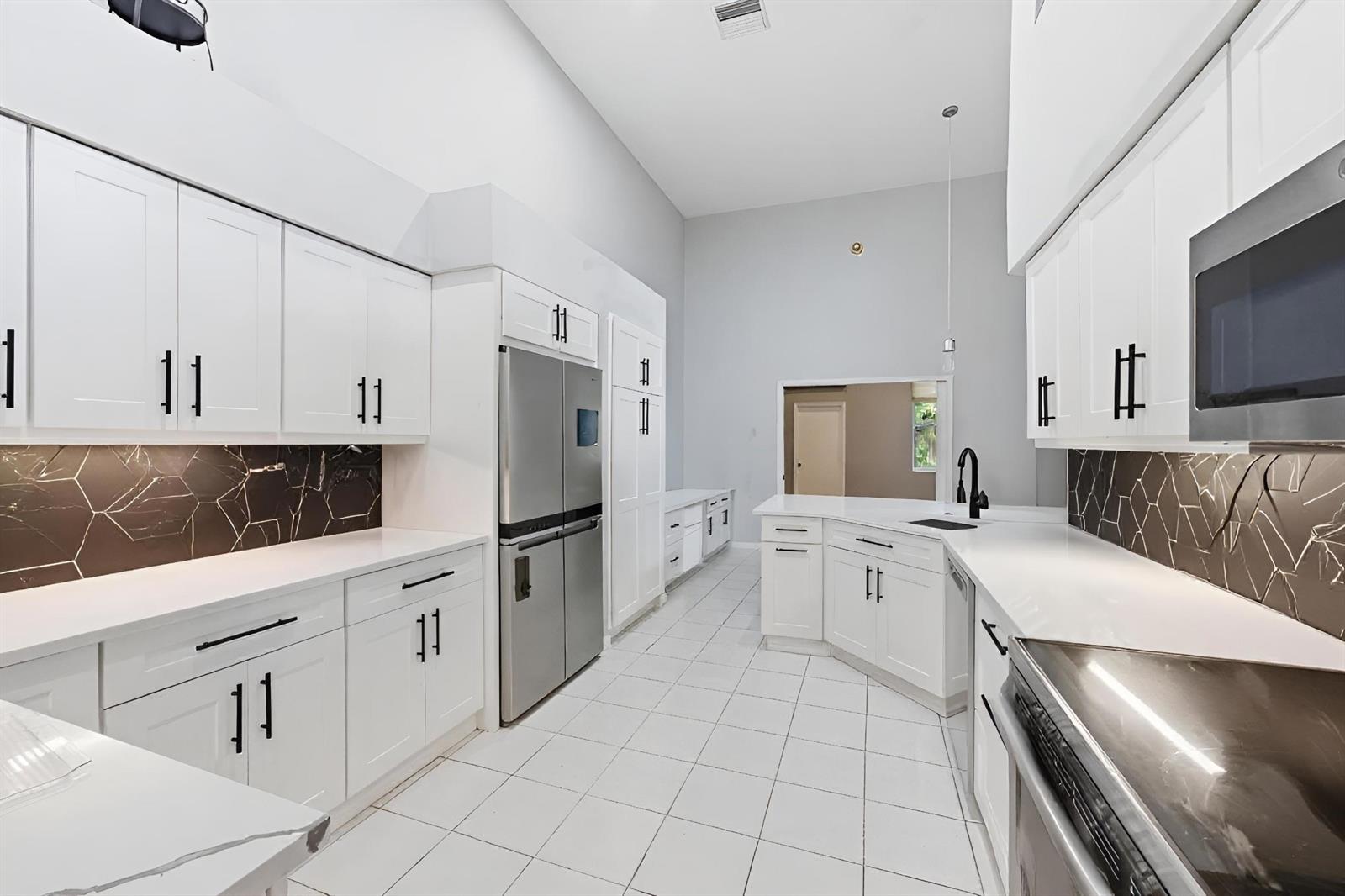 A modern kitchen features white cabinets, stainless steel appliances, and a dark geometric backsplash — 2495 NW 66th Drive, Boca Raton FL 33496, BOCA RATON, FL