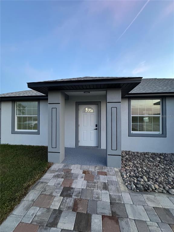 The exterior of a house features a gray stucco facade, a white front door, and pavers — 2555 W TAUNTON ROAD, AVON PARK, FL
