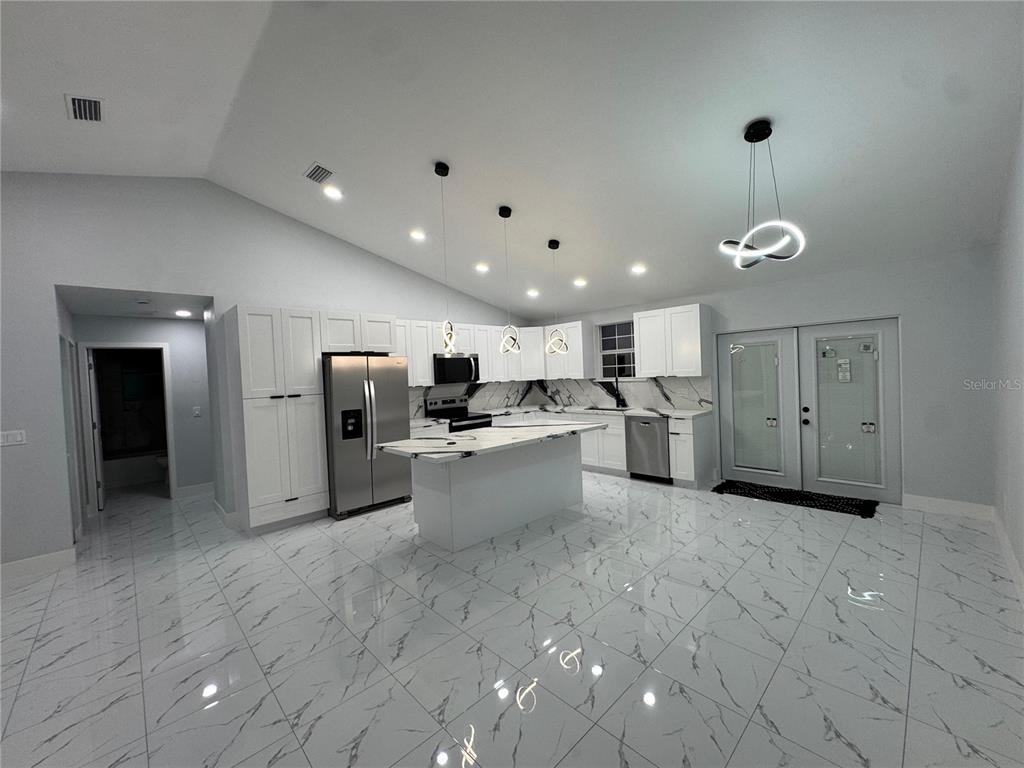 A modern kitchen features white cabinetry, a marble-topped island, and white marble-patterned tile flooring — 2555 W TAUNTON ROAD, AVON PARK, FL