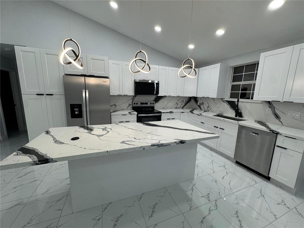 A modern kitchen features white cabinets, marble-patterned countertops, a large island, and stainless steel appliances — 2555 W TAUNTON ROAD, AVON PARK, FL