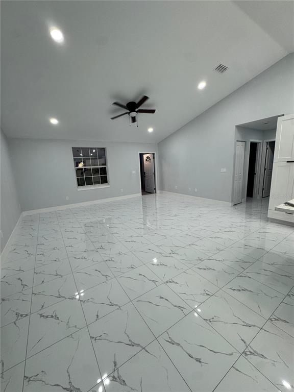 A spacious room features white marble-look tile flooring, a vaulted ceiling with a fan, and recessed lighting — 2555 W TAUNTON ROAD, AVON PARK, FL