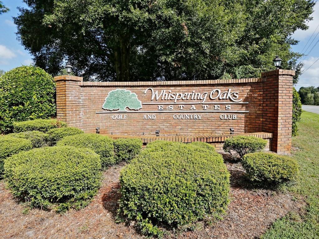 A brick monument sign for Whispering Oaks Estates Golf and Country Club sits outdoors — 35077 WHISPERING OAKS BOULEVARD, DADE CITY, FL