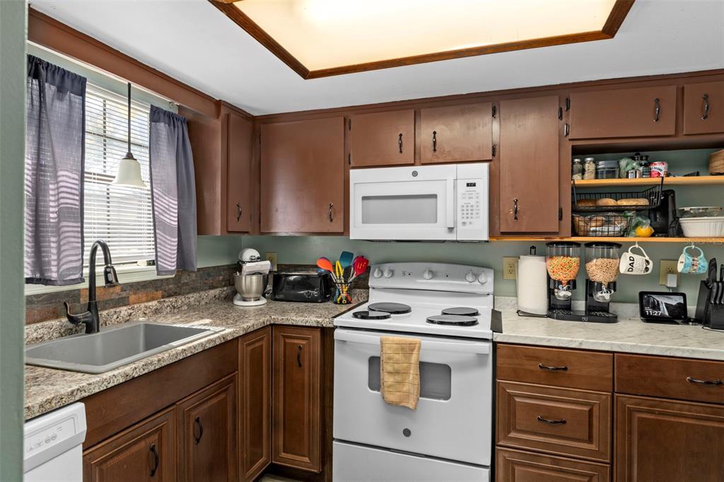 A kitchen with brown cabinets, white appliances, a granite countertop, and a window with curtains — 35077 WHISPERING OAKS BOULEVARD, DADE CITY, FL
