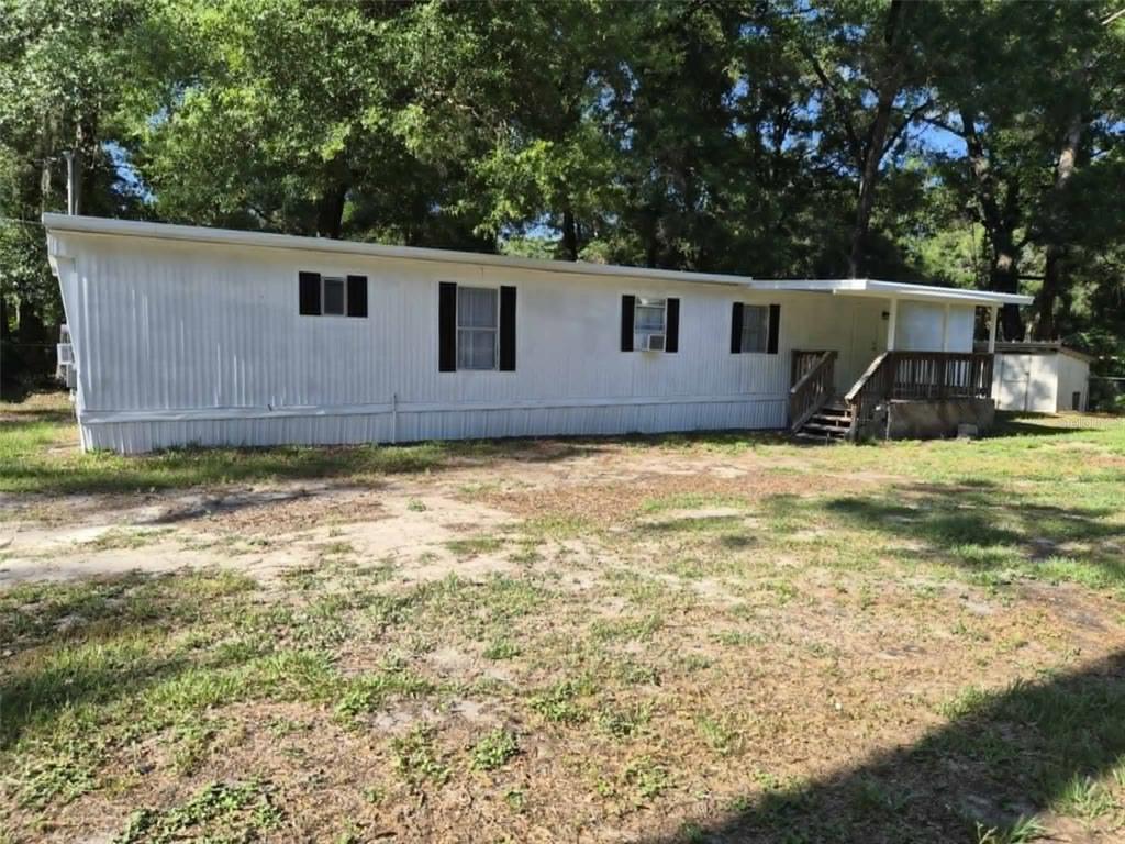 A white mobile home with black shutters and a wooden deck sits on a lot — 201 NW 135TH AVENUE, OCALA, FL