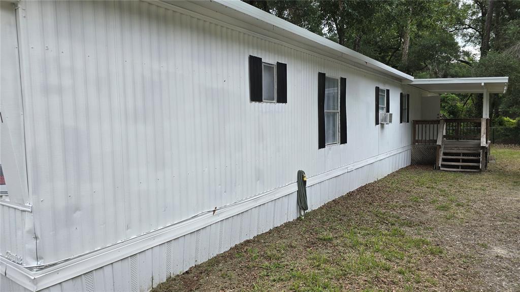A side view of a white mobile home with black shutters and a wooden porch — 201 NW 135TH AVENUE, OCALA, FL
