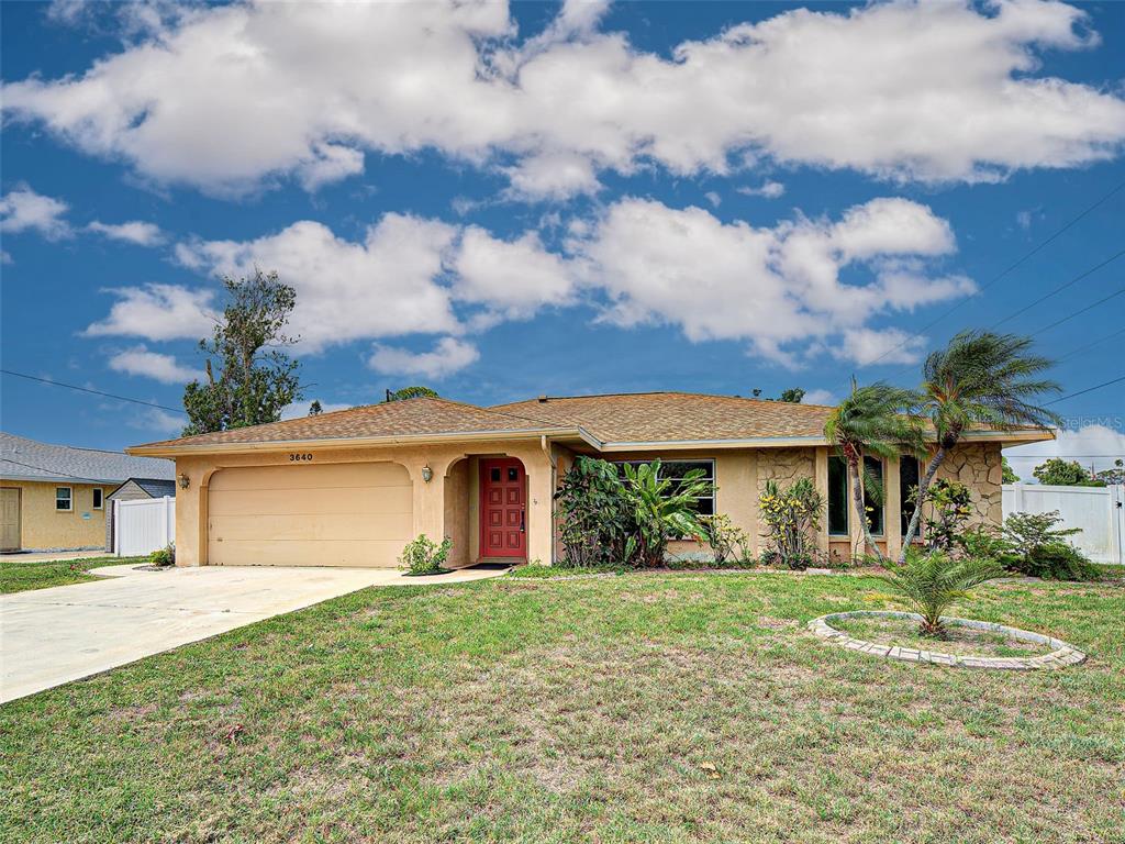A single-story house with a tan stucco exterior, a red front door, and a two-car garage — 3640 STERLING ROAD, VENICE, FL