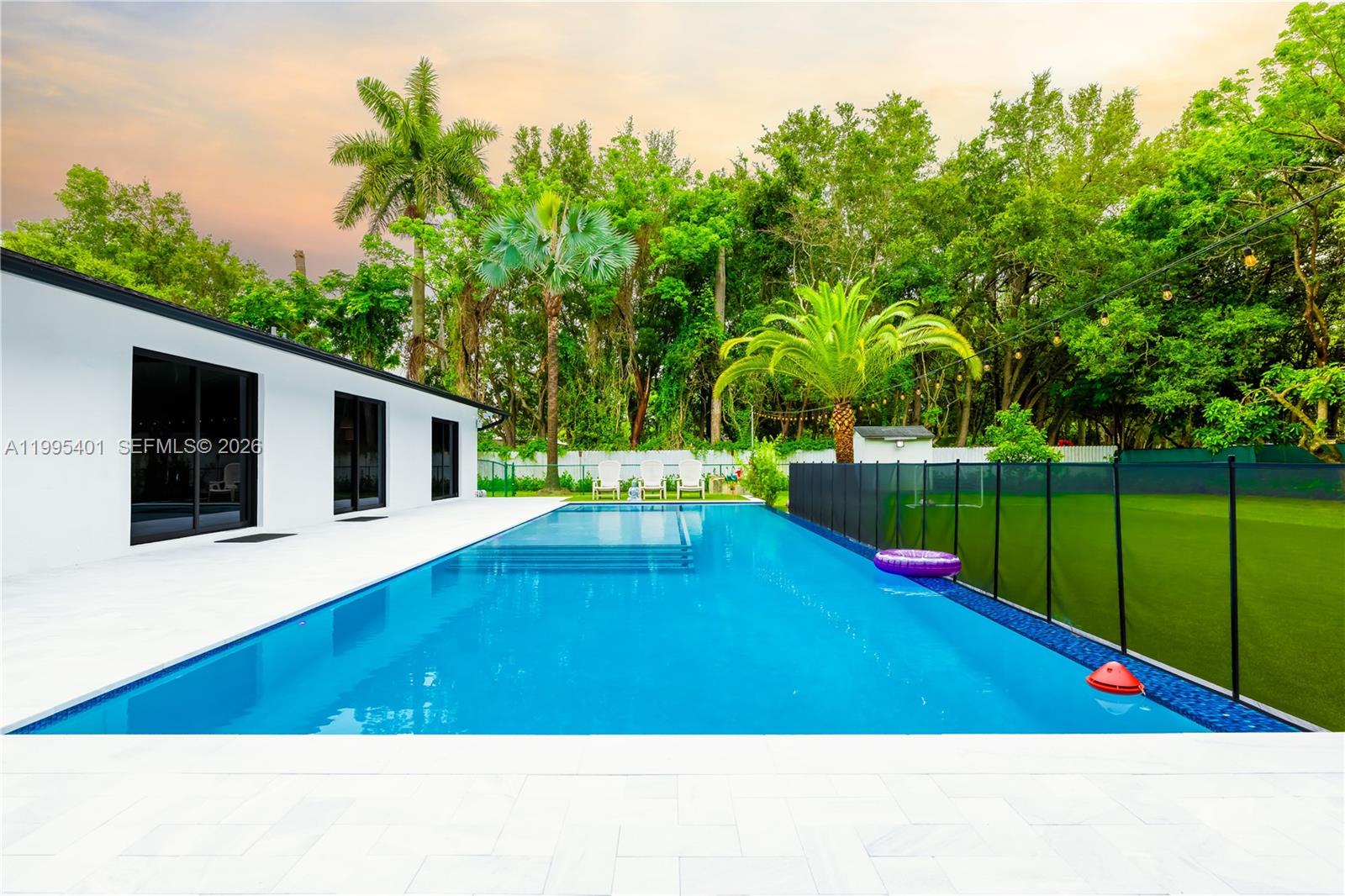 A modern white house features a long rectangular swimming pool with a black safety fence — 18840 SW 218th St, Miami FL 33170, MIAMI, FL