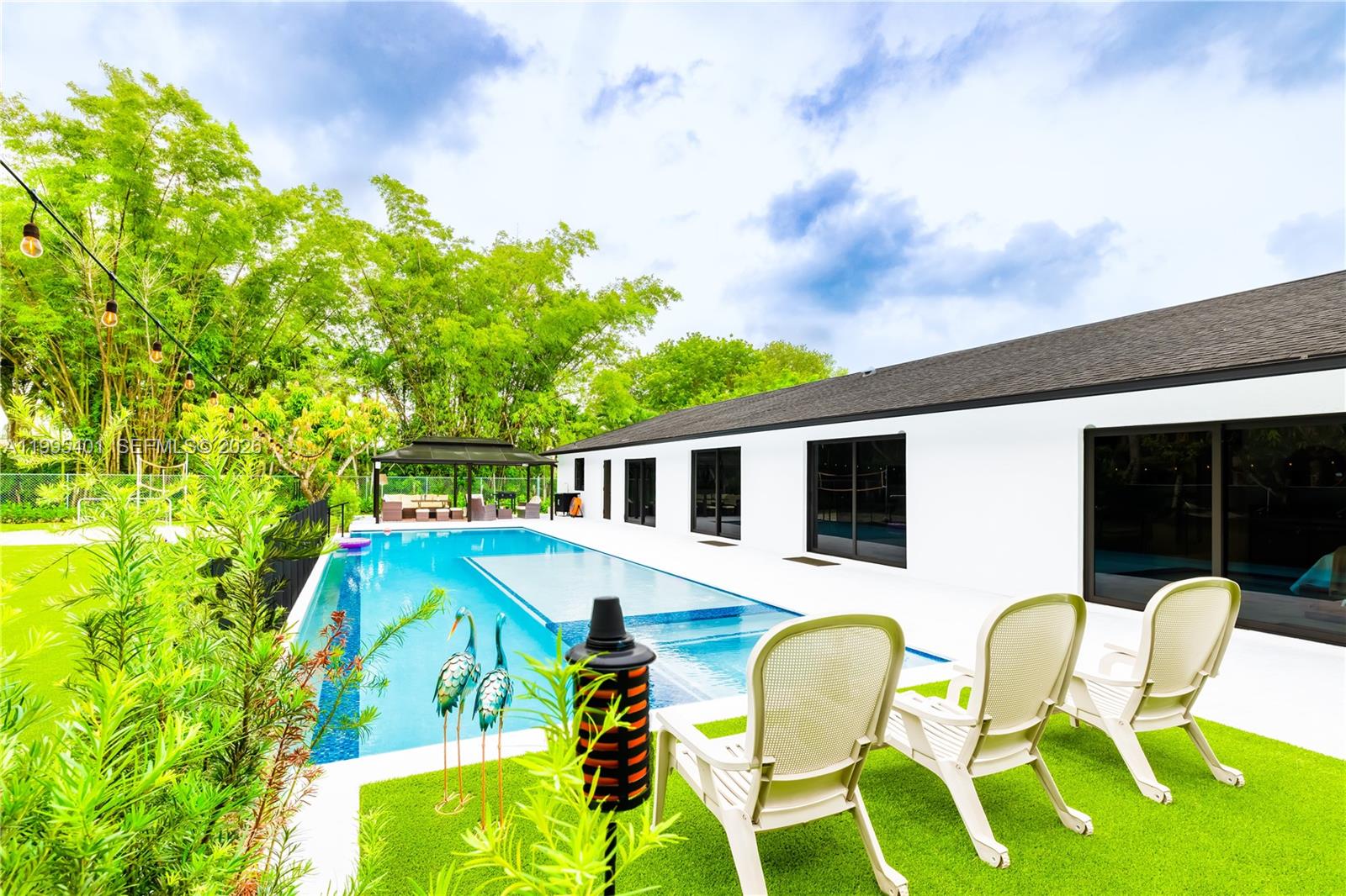 A backyard features a rectangular swimming pool, a patio with three chairs, and bamboo trees — 18840 SW 218th St, Miami FL 33170, MIAMI, FL