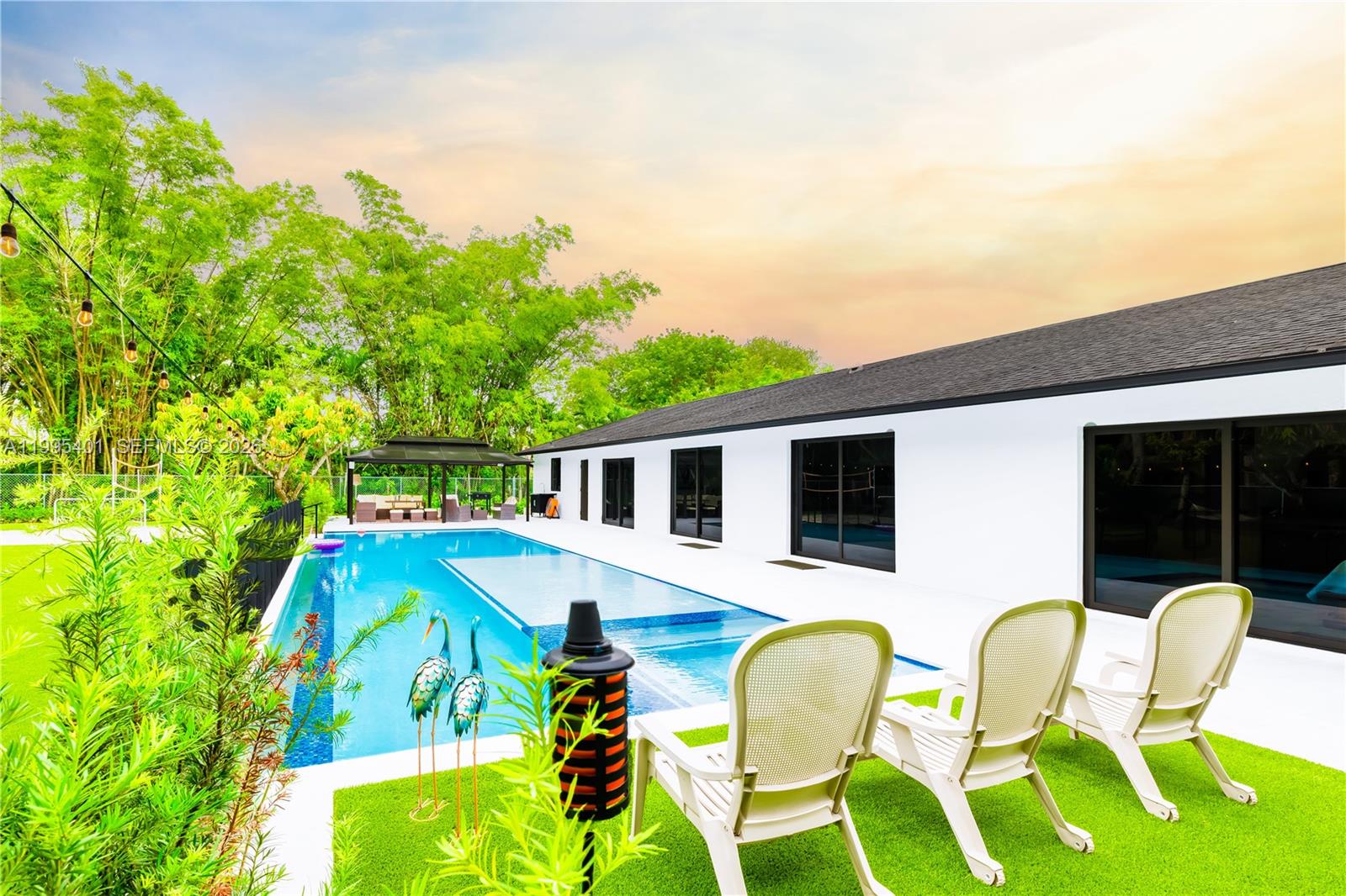 A backyard features a rectangular swimming pool, a patio with three chairs, and lush greenery — 18840 SW 218th St, Miami FL 33170, MIAMI, FL
