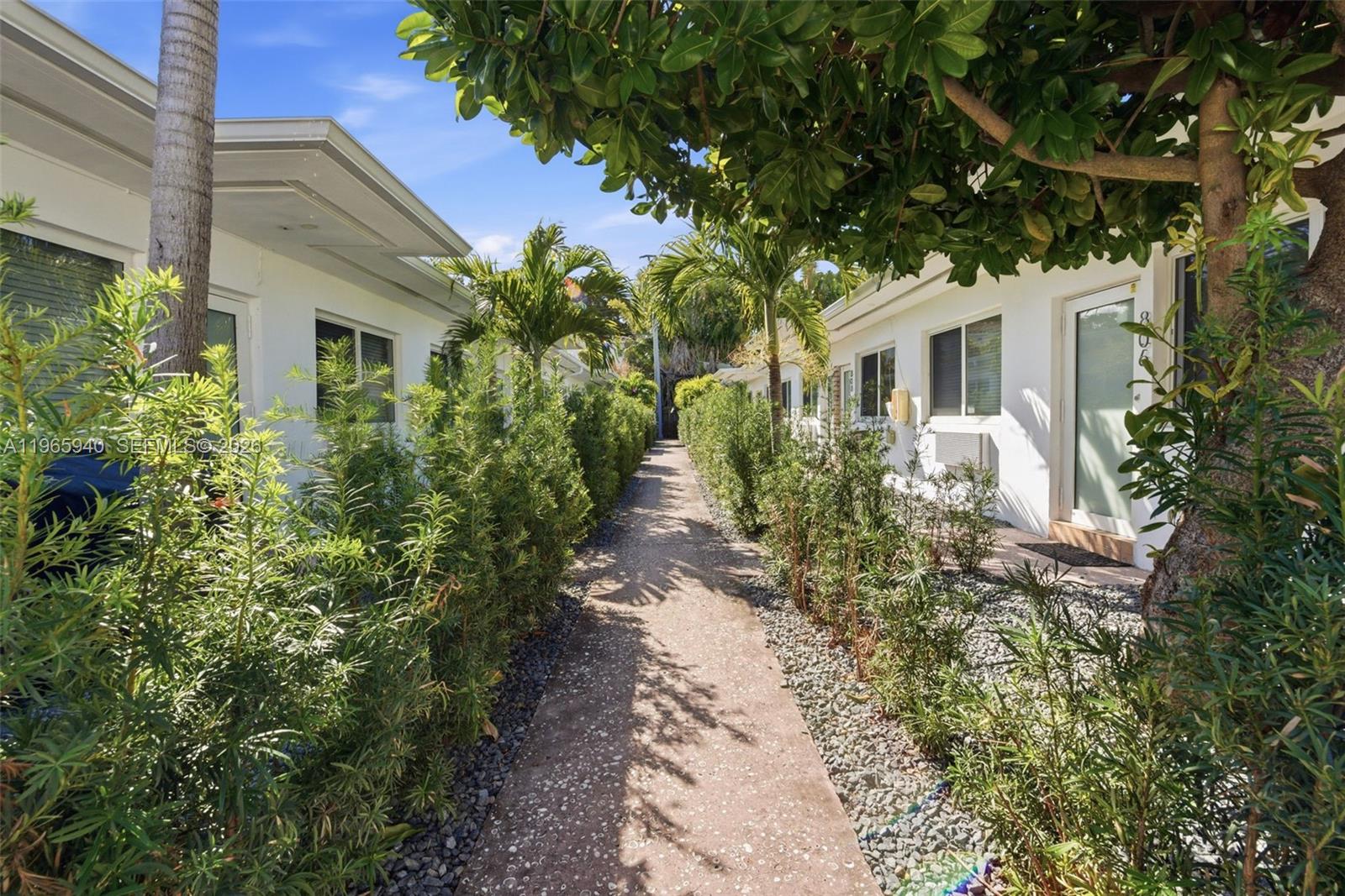 A narrow concrete walkway leads between two white buildings lined with green hedges and trees — 800 85th St, Miami Beach FL 33141, MIAMI BEACH, FL