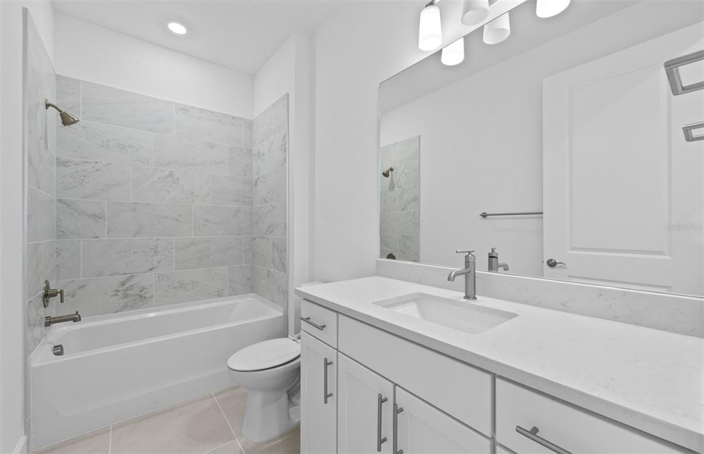 A modern bathroom features a white vanity, a toilet, and a bathtub with marble-look tile — 29028 CORAL HARBOUR DRIVE, ENGLEWOOD, FL