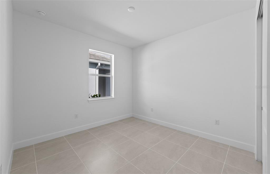 An empty room with white walls, light-colored tile flooring, and a single window — 29028 CORAL HARBOUR DRIVE, ENGLEWOOD, FL