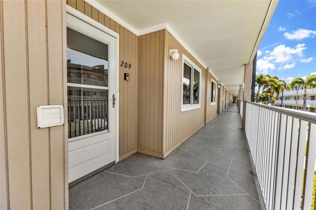 An exterior walkway with tan vertical siding, a white door numbered 209, and stone flooring — 150 HARBORSIDE AVENUE UNIT 209, PUNTA GORDA, FL