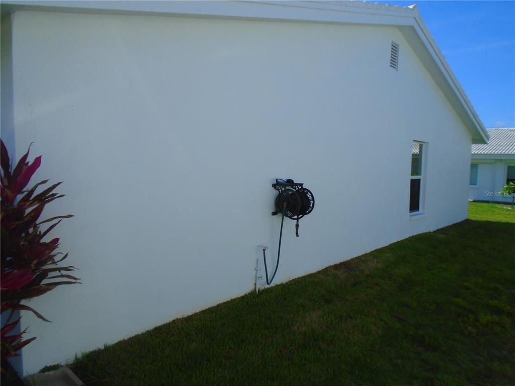 A side view of a white stucco house exterior featuring a wall-mounted hose reel — 3648 91ST AVENUE N UNIT 6, PINELLAS PARK, FL