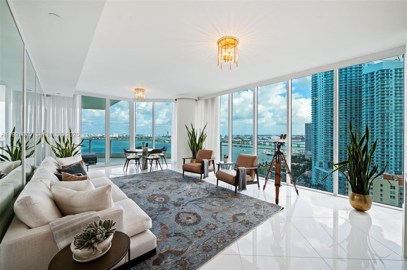 A modern living room features floor-to-ceiling windows, a large patterned rug, and panoramic water views — 2020 N Bayshore Dr # 2502, Miami FL 33137, MIAMI, FL