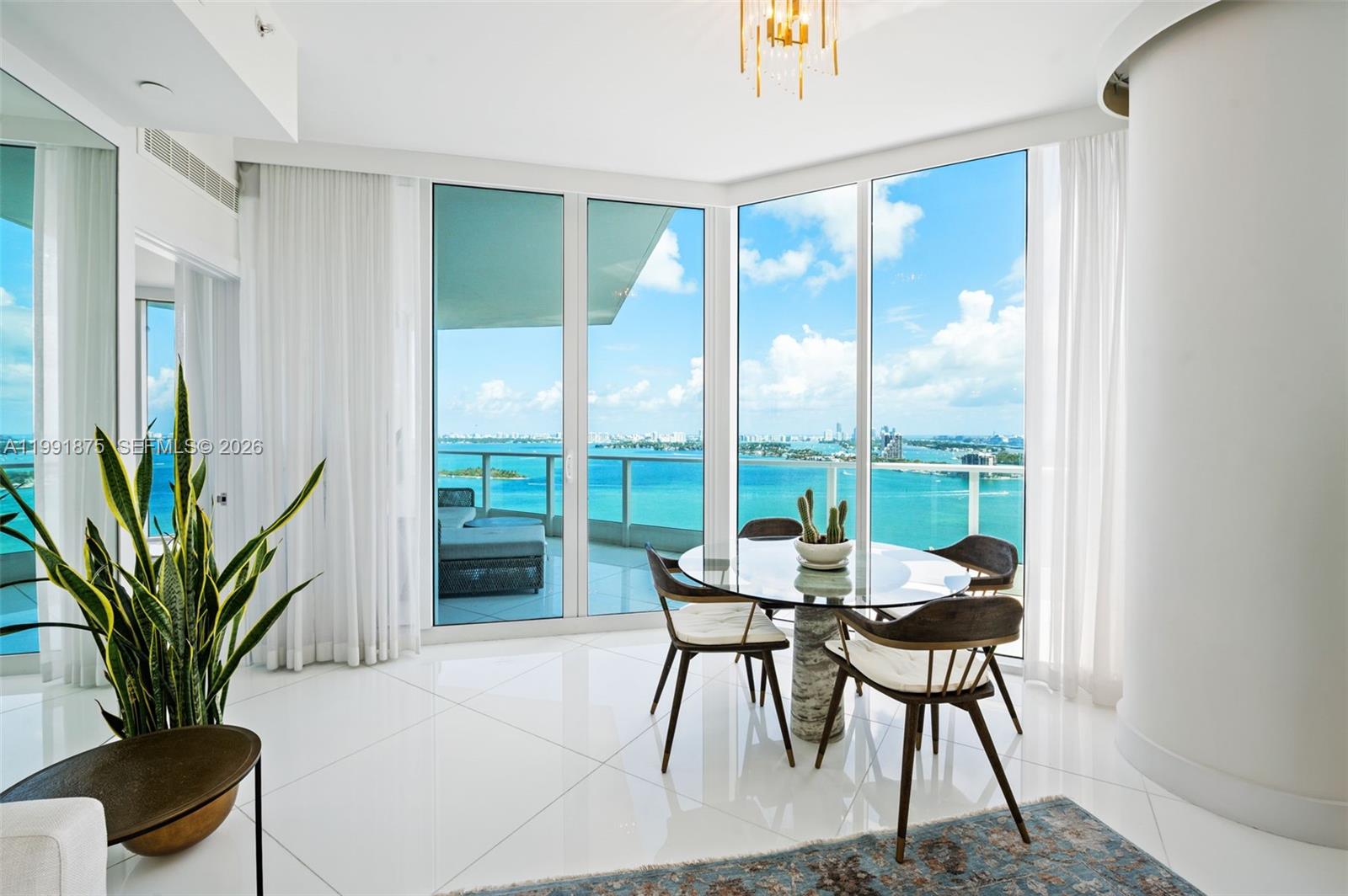 A dining area features a glass table, modern chairs, and floor-to-ceiling windows overlooking the ocean — 2020 N Bayshore Dr # 2502, Miami FL 33137, MIAMI, FL