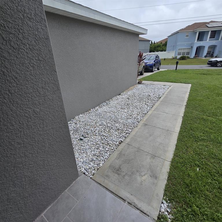 A gray exterior wall sits beside a gravel garden bed and a concrete walkway — 540 BRISTOL CIRCLE, KISSIMMEE, FL