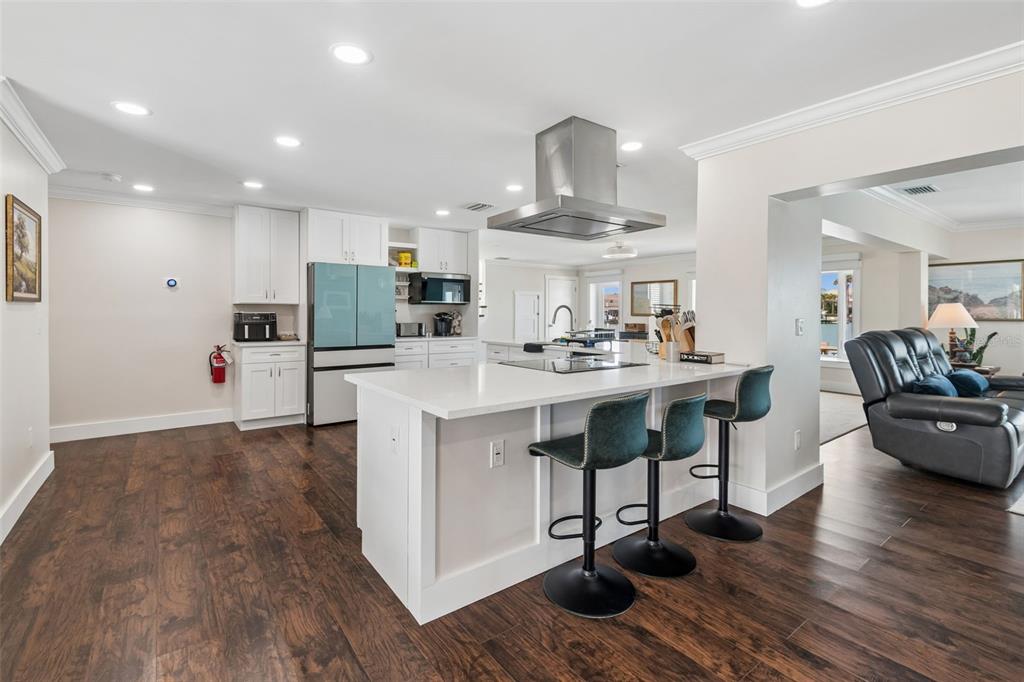 A modern kitchen features white cabinetry, a central island with bar seating, and dark flooring — 478 HARBOR DRIVE N, INDIAN ROCKS BEACH, FL