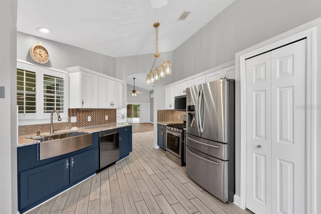 A kitchen features blue lower cabinets, white upper cabinets, stainless steel appliances, and wood-look flooring — 614 JOHN THOMAS AVENUE, DELAND, FL