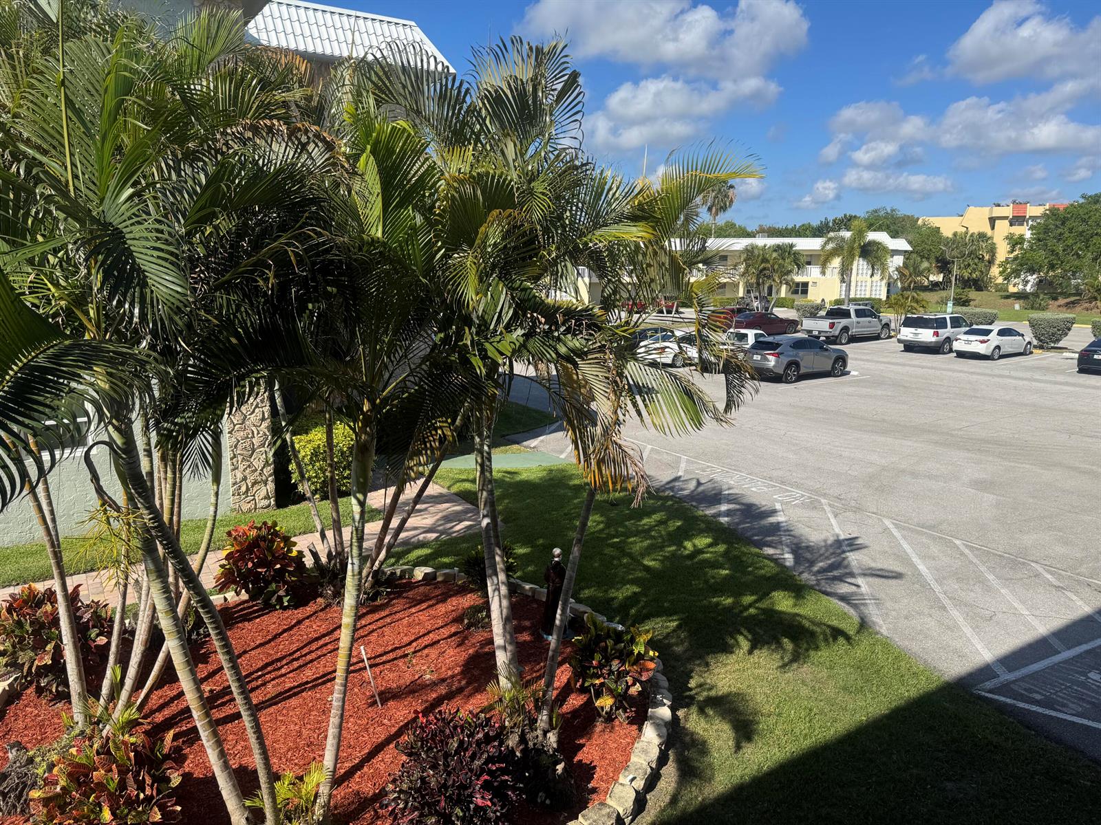 An elevated view of a landscaped garden with palm trees overlooking a paved parking lot — 9818 Marina Boulevard # 1220, Boca Raton FL 33428, BOCA RATON, FL